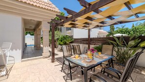 An outdoor patio with a table set for two, surrounded by chairs, under a wooden pergola. - Villa Alex - Charming Kapparis Getaway (Protaras)