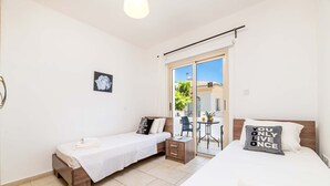 A hotel room with two beds, a small table, and a view of the outside. - Villa Alex - Charming Kapparis Getaway (Protaras)