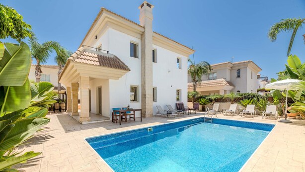 A swimming pool surrounded by lounge chairs and a white building with a tiled roof. - Villa Alex - Charming Kapparis Getaway (Protaras)