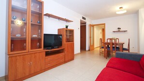 Ein Wohnzimmer mit einer Holzunterhaltungsecke, einem Flachbildfernseher, einem roten Sofa und einem Essbereich mit Holztisch und Stühlen.
