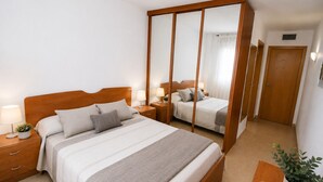 Ein Hotelzimmer mit einem großen Bett, Nachttischen mit Lampen, einem Spiegel, einem Holzschrank und einer Zimmerpflanze.