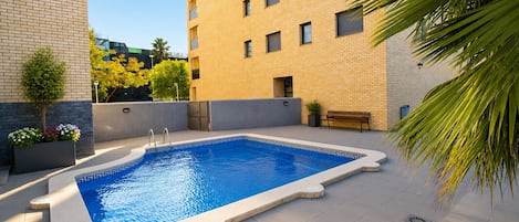 Une piscine rectangulaire bordée de carreaux géométriques, entourée d’une terrasse sur le toit, aménagée avec un banc et des plantes en pot.