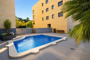 A rectangular swimming pool with a geometric tile border, surrounded by a flat roof terrace with a bench and potted plants. - MAR CAMBRILS Apartment (Cambrils)