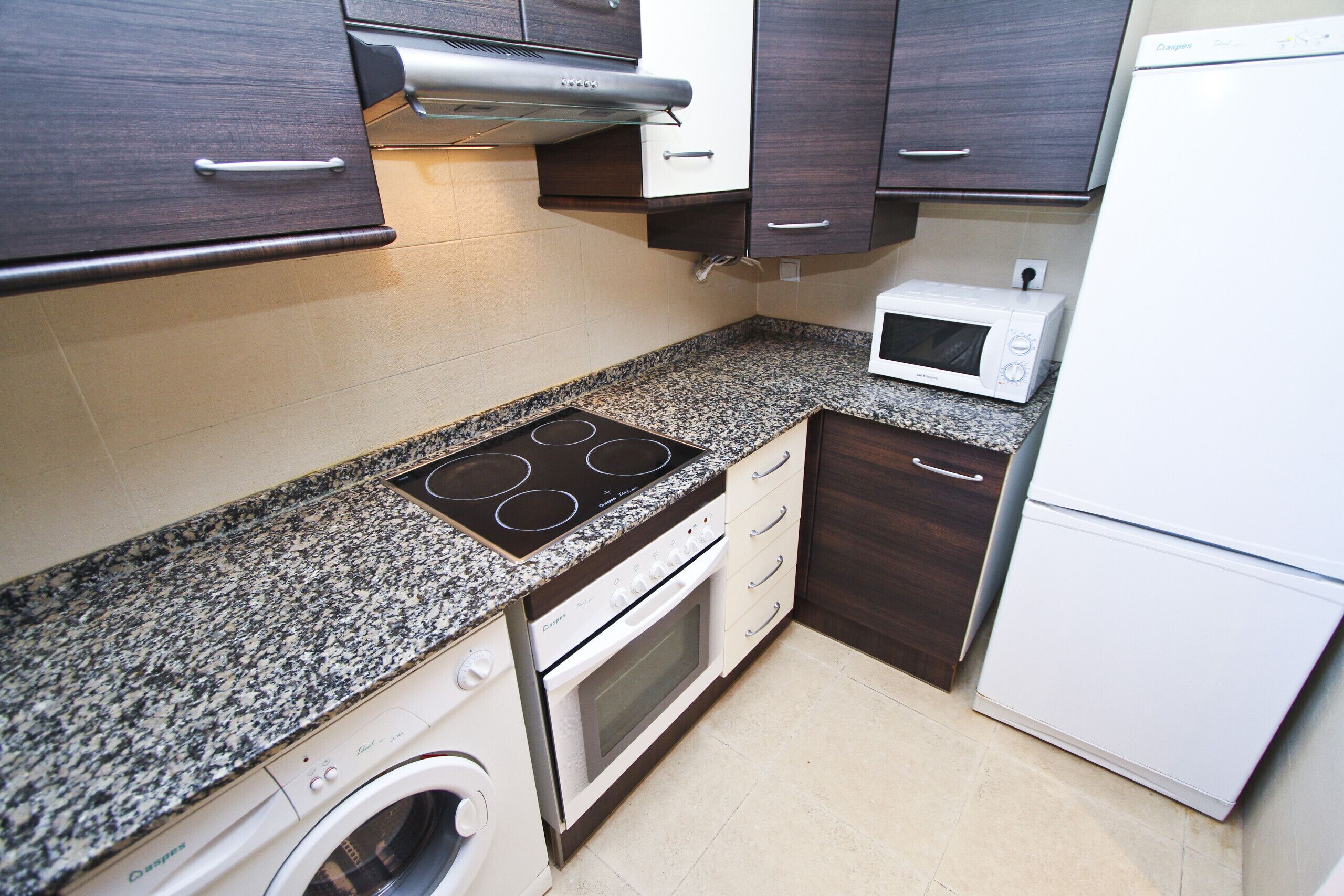 Een compacte keuken met een ingebouwde kookplaat, oven, magnetron en een wasmachine.