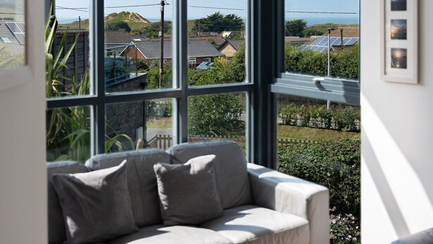 Ein modernes Wohnzimmer mit einem großen Fenster, das Blick auf eine Wohngegend und das Meer gewährt.