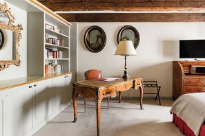 A room with a wooden desk, bookshelves, a television, and a bed.