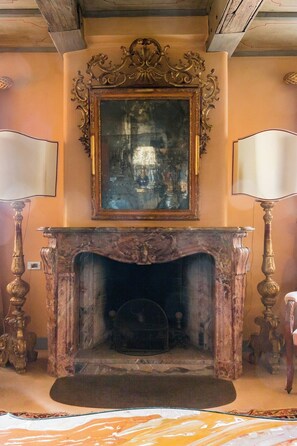 A room with a fireplace, ornate mirror, and two lamps.