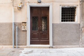 Une porte à deux battants de couleur marron, ornée de motifs décoratifs, une petite fenêtre avec un grillage métallique et un coffret électrique fixé au mur.
