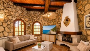 Une pièce aux murs de pierre, dotée d’une cheminée, d’un canapé, d’un téléviseur et d’une grande fenêtre.