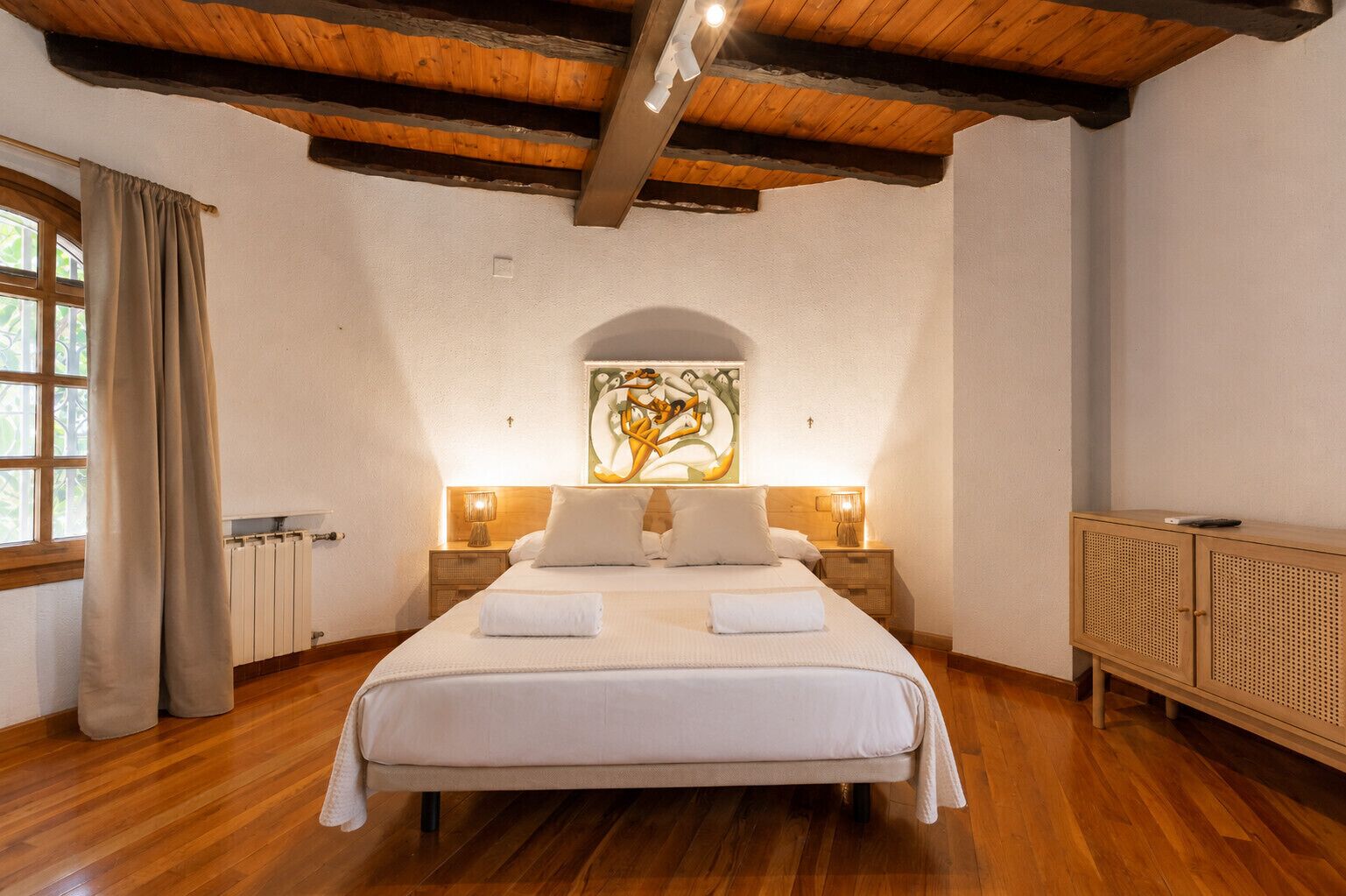 Ein Schlafzimmer mit einem großen Bett, Holzboden, einem Heizkörper, einem Gemälde und einem Holzschrank.