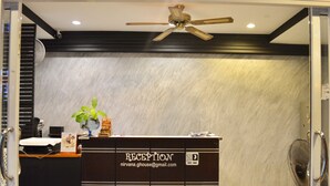 A reception desk with a sign reading "RECEPTION" and an email address. There is a ceiling fan above the desk, and a plant is placed on the counter. - Nirvana Guesthouse (Koh Tao)