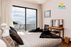 A bedroom with a large bed, a desk, and a view of the sea. - Contemporary villa, infinity pool | Designhouse (Arco Da Calheta)