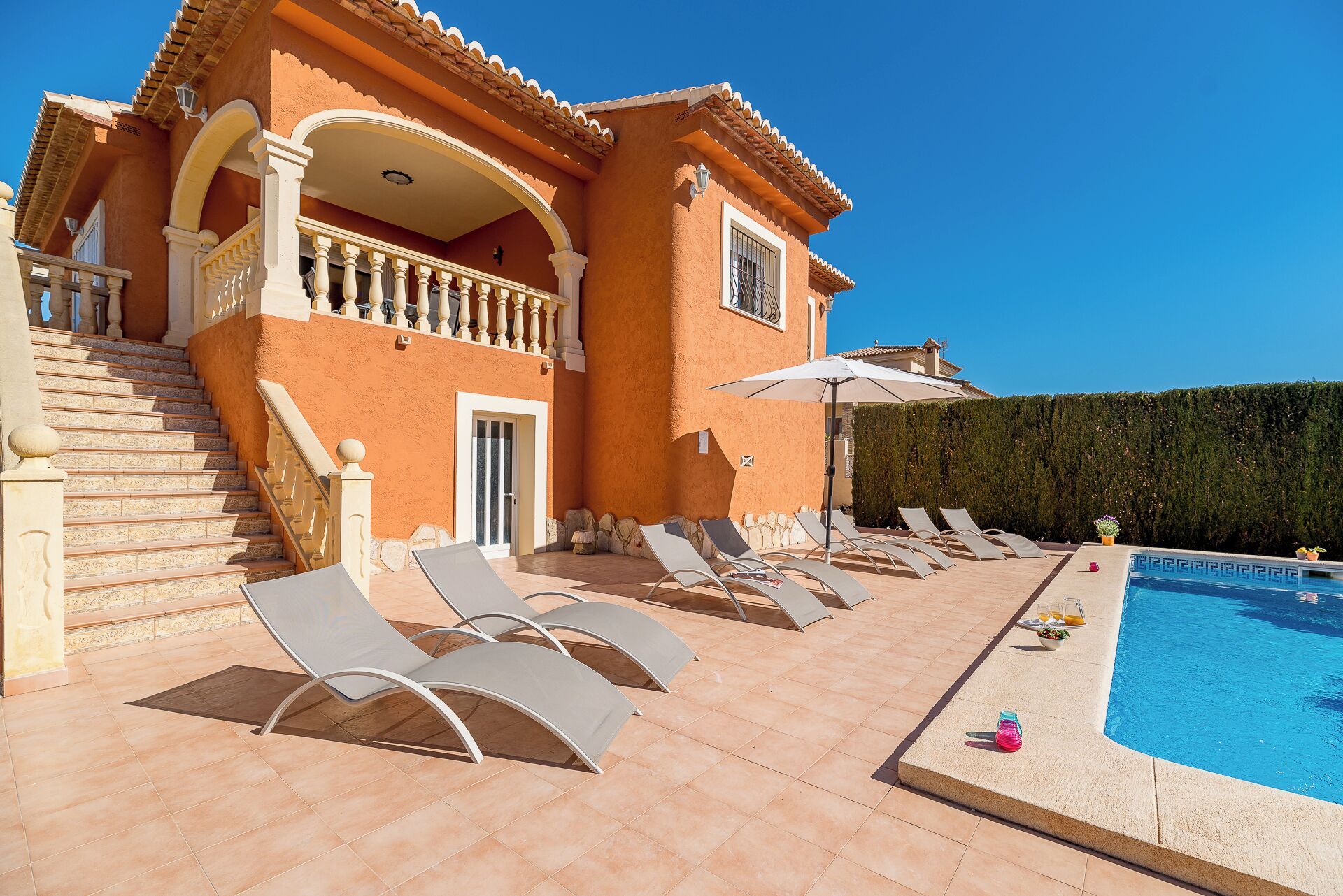 A villa with a swimming pool, sun loungers, and a staircase leading to a balcony.