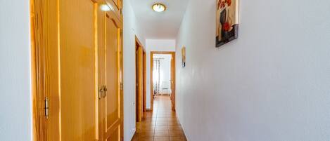 Un couloir avec des portes en bois, un sol carrelé et un luminaire au plafond.