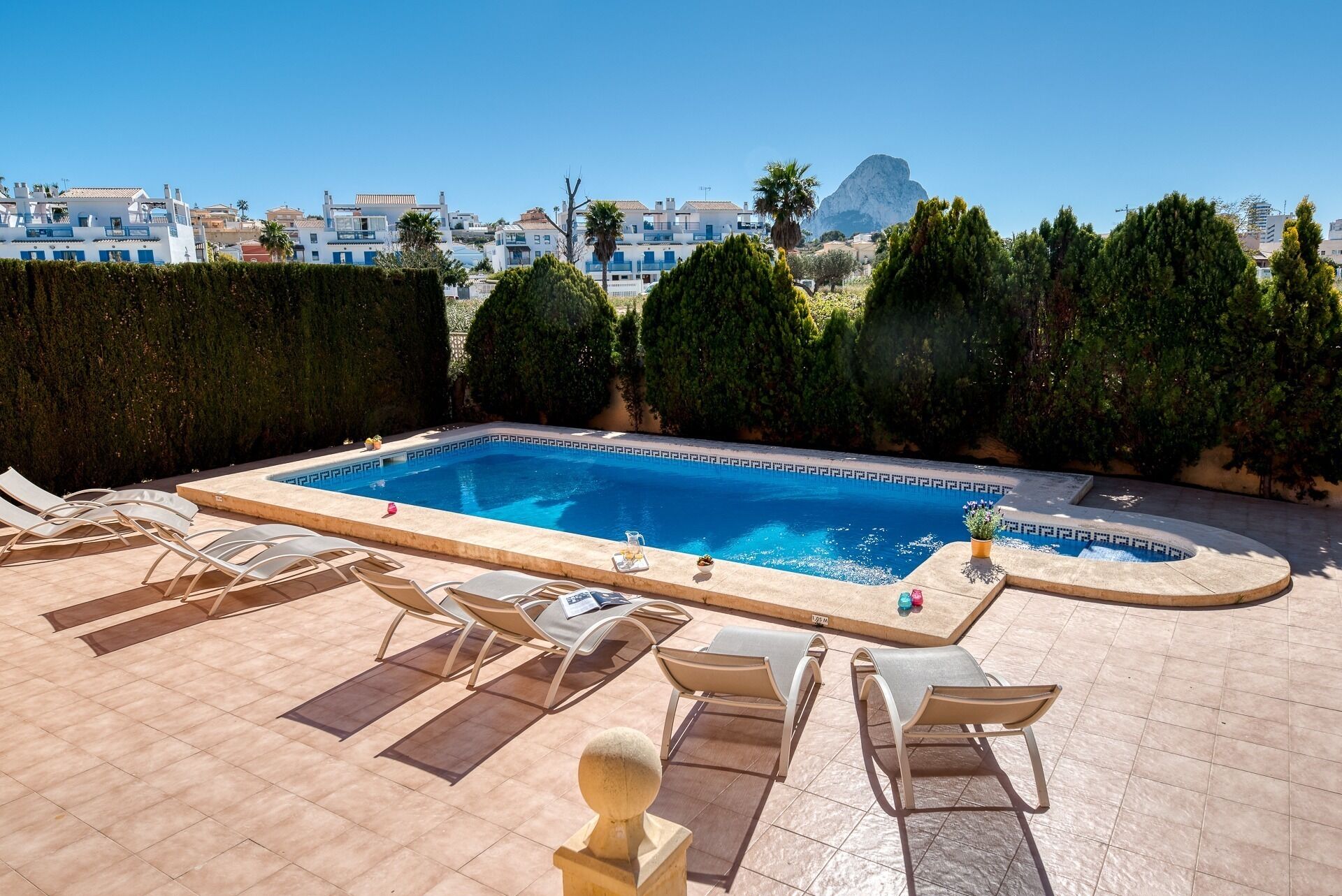 Piscina rectangular con una característica de agua azul cristalina, rodeada de sillas de descanso y una pequeña mesa con un bandejón para bebidas.