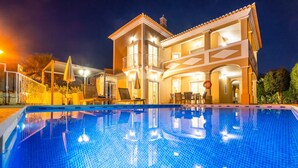 A swimming pool with a clear blue water surface, surrounded by a building with multiple balconies and a covered patio area. - Villa with Heatable Pool and BBQ in Albufeira (Albufeira)