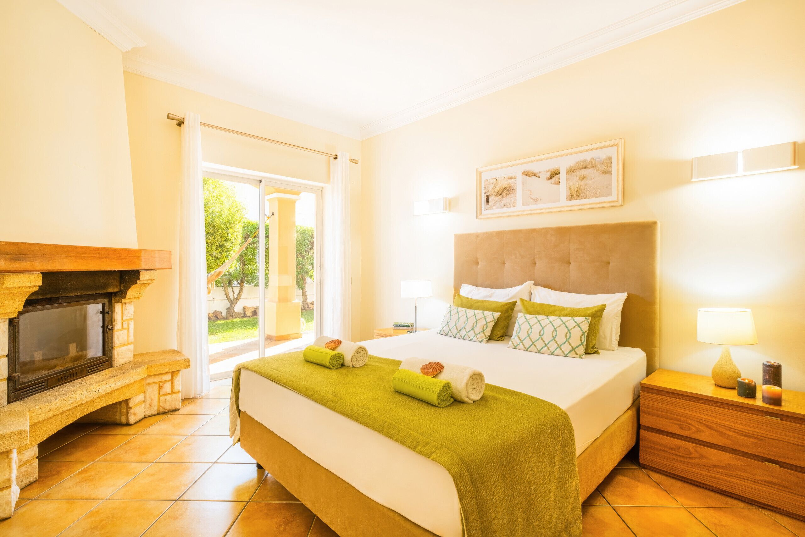 A hotel room with a bed, a fireplace, a nightstand, and a view of the outdoors.