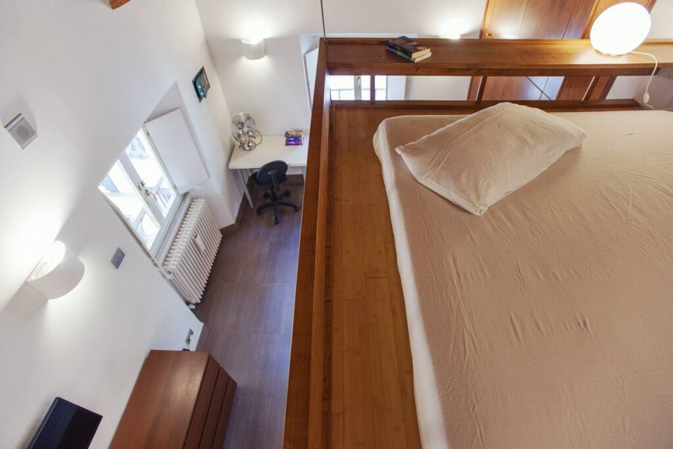 Une chambre à coucher avec une tête de lit en bois, un lit avec un oreiller, un bureau avec une chaise et un radiateur.