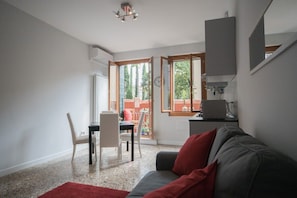 Una sala de estar moderna con un sofá gris, una mesa de comedor con sillas y una zona de cocina con estufa y lavaplatos.