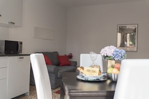 Un comedor con una mesa dispuesta para dos, microondas, sofá y un jarrón con flores.