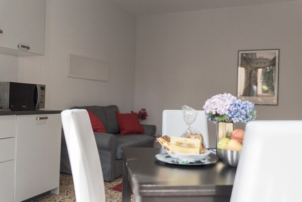 A dining area with a table set for two, a microwave, a sofa, and a vase with flowers. - Venier Apartment (Venice)