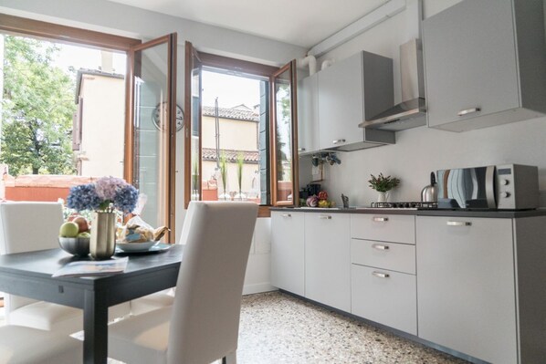 A modern kitchen with white cabinets, a stainless steel range hood, and a dining area with a table and chairs.