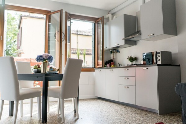 A compact kitchen with white cabinets, a microwave, and a dining area with two chairs and a table.