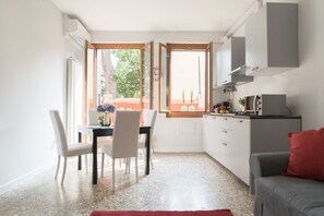 A compact kitchen with a dining area, a red rug, and a grey sofa.