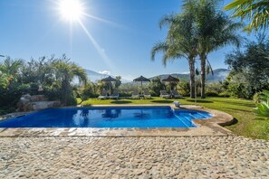 A swimming pool with lounge chairs and umbrellas, surrounded by greenery and mountains.