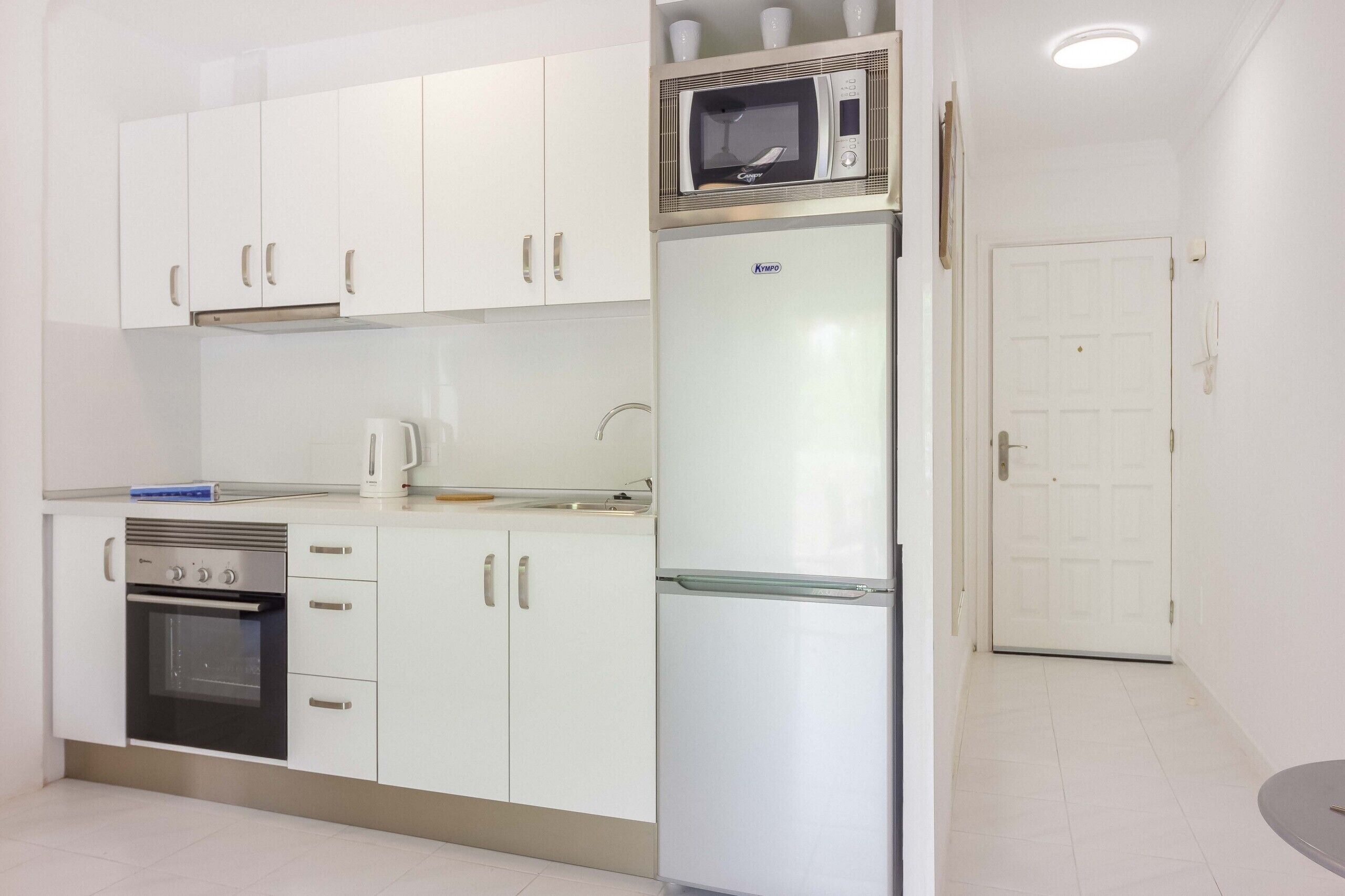 A compact kitchen with white cabinets, a built-in oven, a microwave, and a refrigerator.
