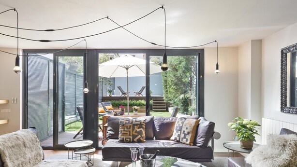A modern living room with a sofa set, a glass coffee table, and a dining area with outdoor seating.