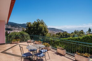 A balcony with a table and chairs, potted plants, and a view of a cityscape and mountains. - Great family villa in Funchal | Casa Petronella (Funchal)