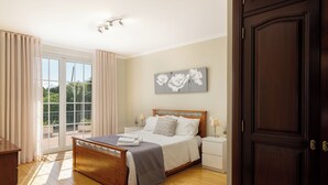 Ein Schlafzimmer mit einem hölzernen Bett, einem Nachttisch, einer Lampe, einem Fenster mit Vorhängen und einer Tür.