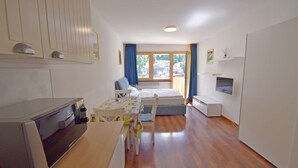 A compact hotel room with a kitchenette, a bed, a small table, and a window with curtains. - EMERALD 36 STUDIO 022143-AT-672307 (Madonna di Campiglio)