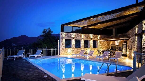 A swimming pool with lounge chairs and a stone wall, surrounded by a wooden deck. - Villa Rachi - Four Bedroom Villa, Sleeps 8 (Rachi)