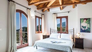 A bedroom with a bed, a nightstand, a window with curtains, and a painting on the wall. - Villa Rachi - Four Bedroom Villa, Sleeps 8 (Rachi)
