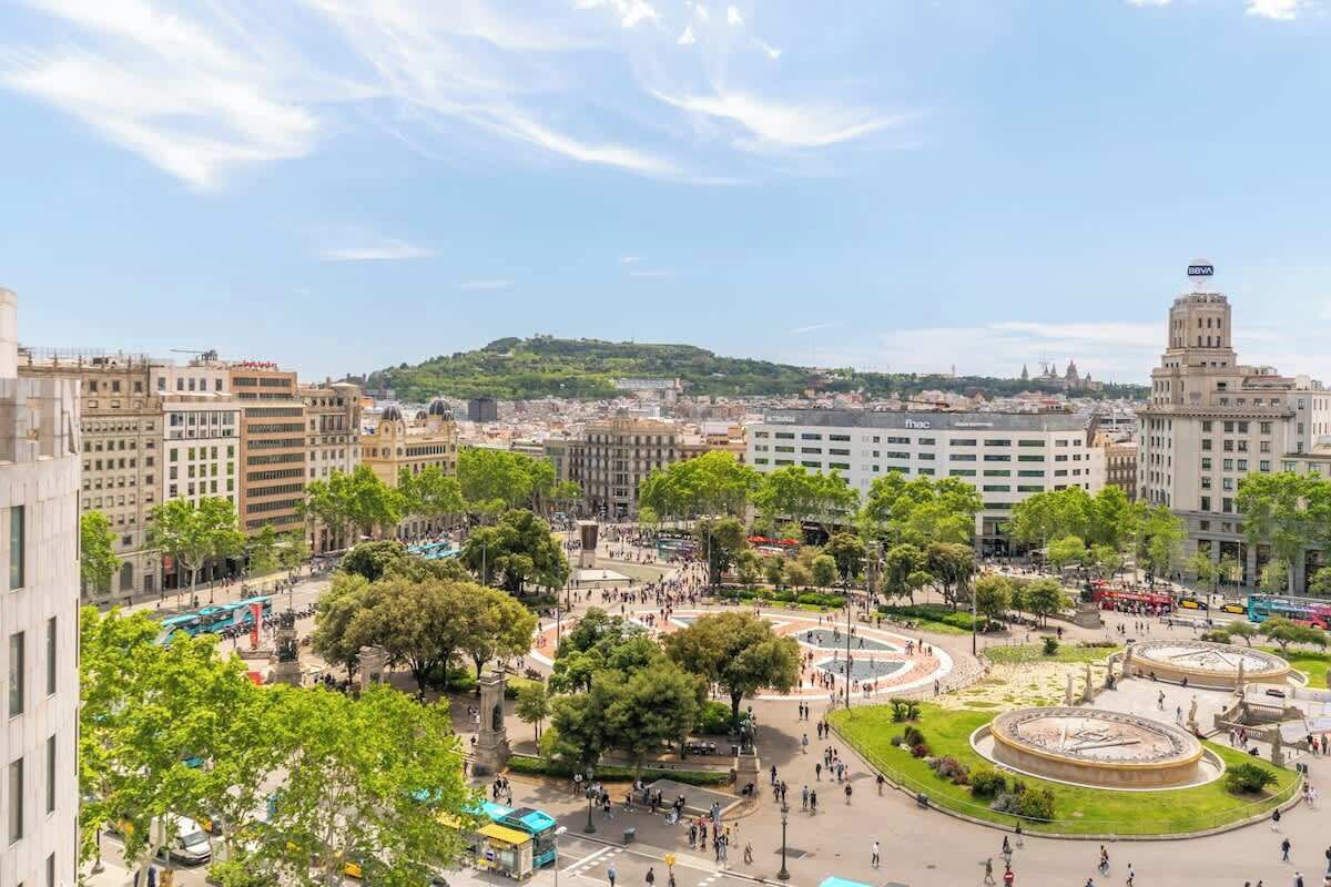 Ein Stadtplatz mit einer zentralen Fontäne, umgeben von Bäumen und Gebäuden.