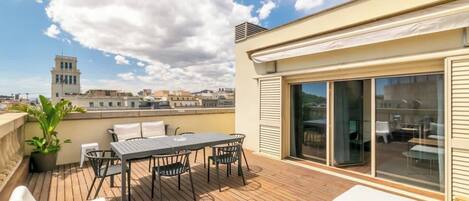 A rooftop terrace with a wooden deck, a table with chairs, a potted plant, and a view of the cityscape.
