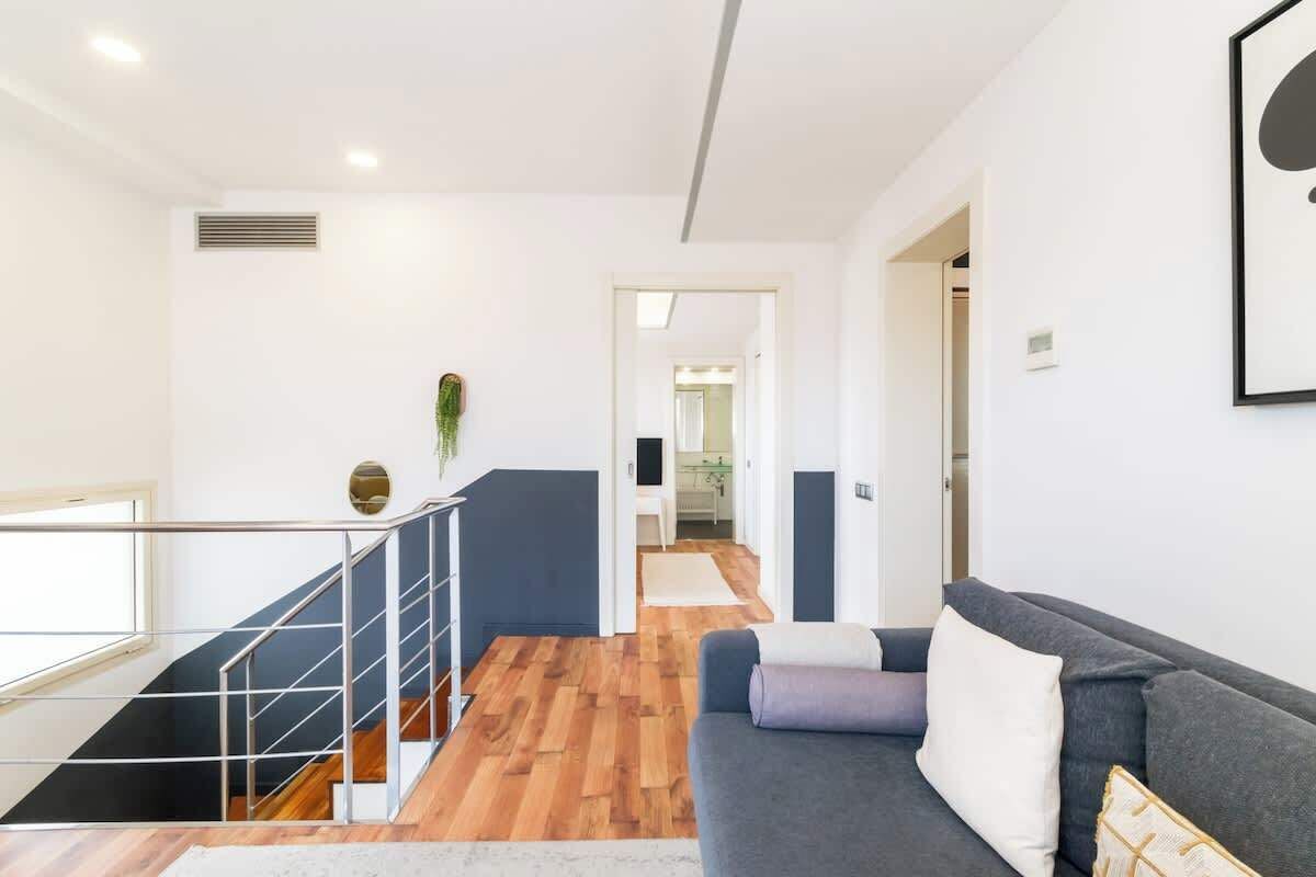 A modern living room with a staircase, a sofa, and a view into the kitchen.