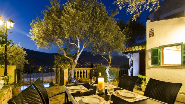 An outdoor dining area with a table set for two, surrounded by chairs, a candle, and a view of the night sky and distant hills. - Coster Catalanet, Villa On The Edge Off Pollença With Amazing Views ETV 1808 (Pollença)