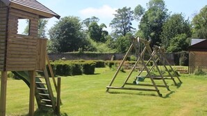 Een houten speeltuintje met een ladder, een schommel en een verzorgd gazon.
