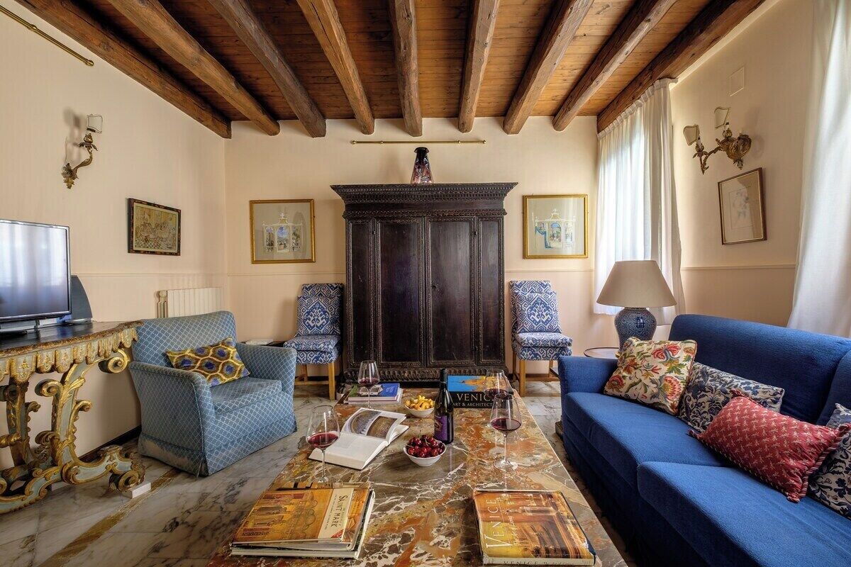 Un soggiorno con divano, poltrone, un tavolino con libri e bicchieri da vino, televisore e camino.