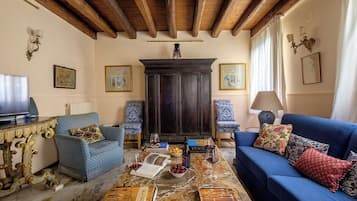 Un soggiorno con divano, poltrone, un tavolino con libri e bicchieri da vino, televisore e camino.