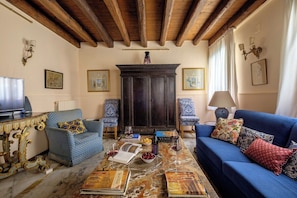 A living room with a sofa, armchairs, a coffee table with books and wine glasses, a television, and a fireplace. - Casa Dell'Albero (Venice)