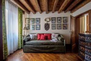 Ein Zimmer mit Holzboden, einer Couch mit Kissen, einer Wand mit gerahmten Bildern und einem Holzkabinett.