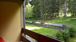 Un balcone con una sedia rossa, con vista su una zona boschiva e un piccolo edificio.