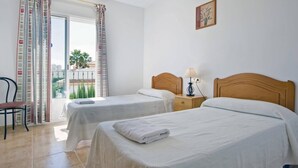 A hotel room with two beds, a chair, a nightstand with a lamp, and a window with curtains. - Villa Senieta - PlusHolidays (Calpe)