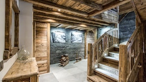 Un interior rústico con vigas de madera a la vista, pared de piedra y escalera de madera.