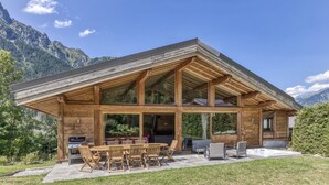 Una cabaña de madera con un amplio patio, mobiliario exterior y vistas a la montaña.