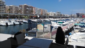 A marina with boats docked, a waterfront promenade, and buildings in the background. - Sunrise watching Tabarca (Santa Pola)